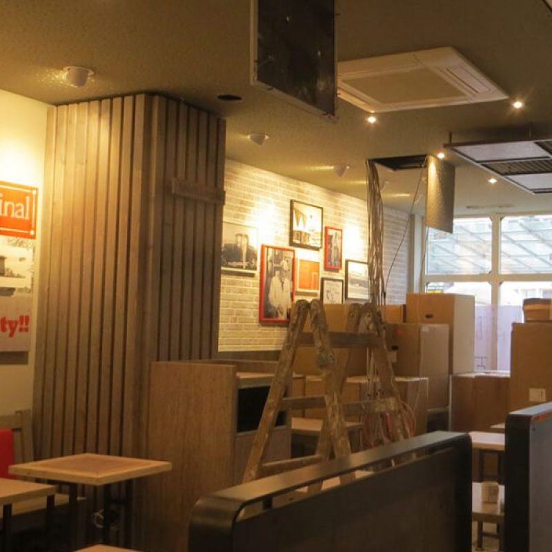 Ein Restaurant mit Kisten und einer Leiter, Wände mit Bildern dekoriert, Tische und Stühle aufgestellt, aber noch im Umbau