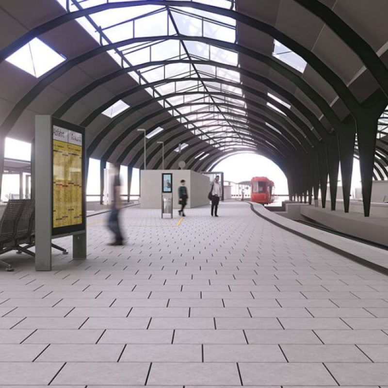 Modern Bahnhof mit gewölbtem Dach, gepflastertem Boden, Sitzgelegenheiten und einem roten Zug im Hintergrund. Menschen bewegen sich durch die Halle